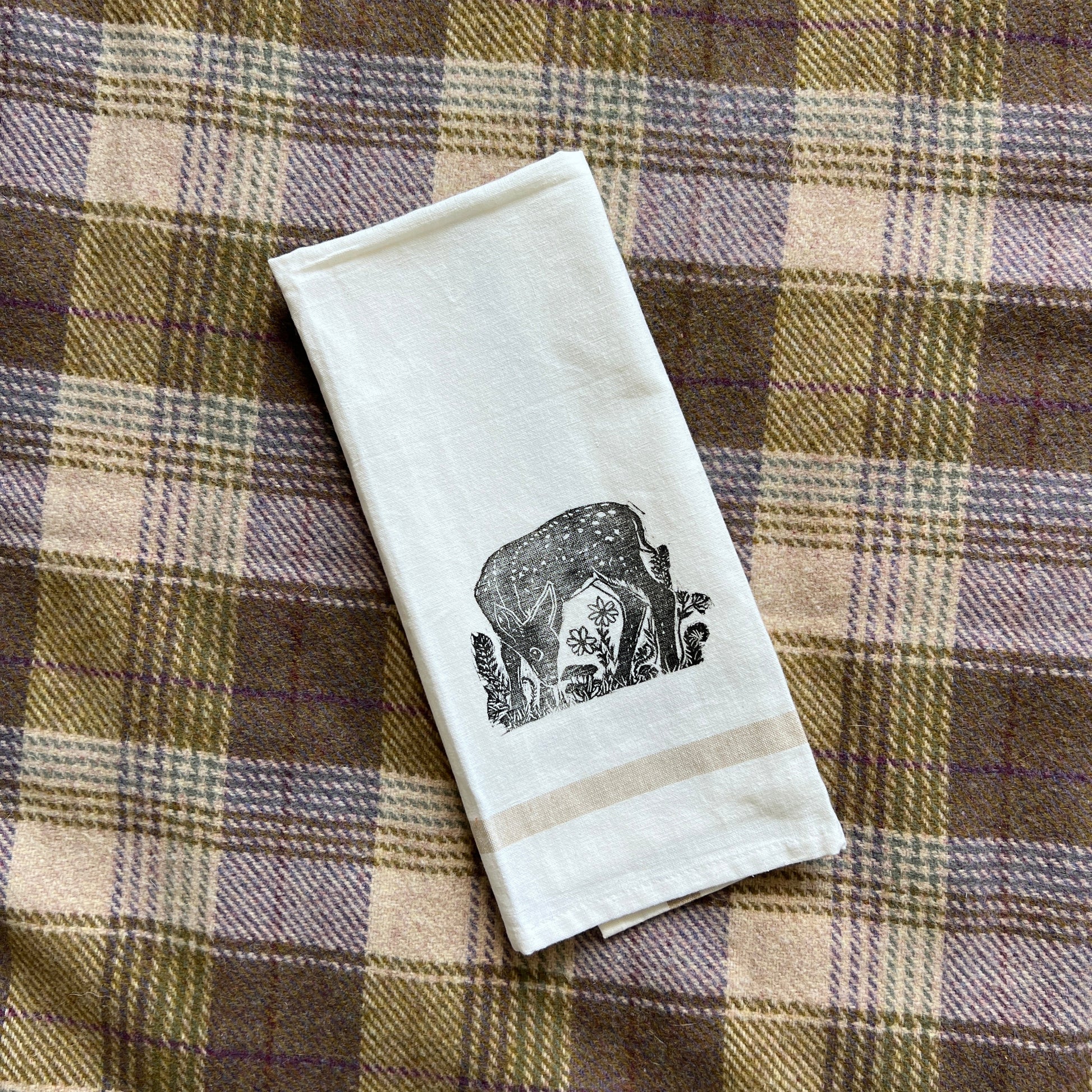 White towel with a black stamped fawn design on a plaid fabric background