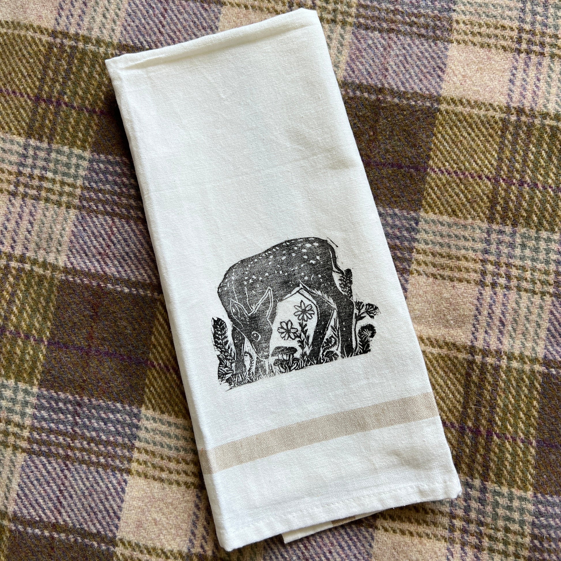 White tea towel with black fawn design on a plaid fabric background