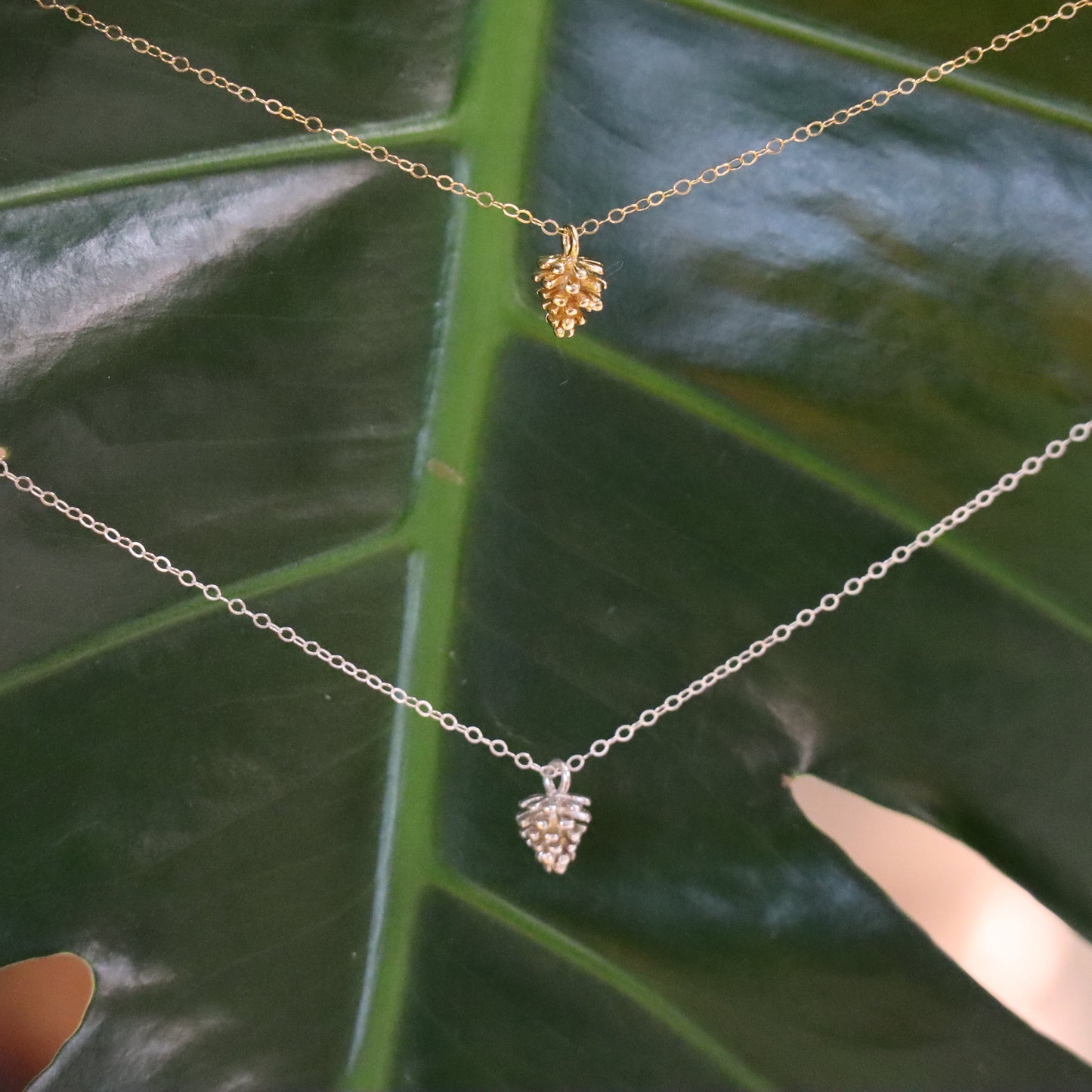 two necklaces with pinecone pendants