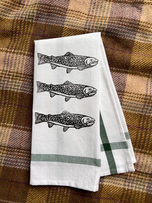 Folded white towel with black fish design on a plaid fabric background