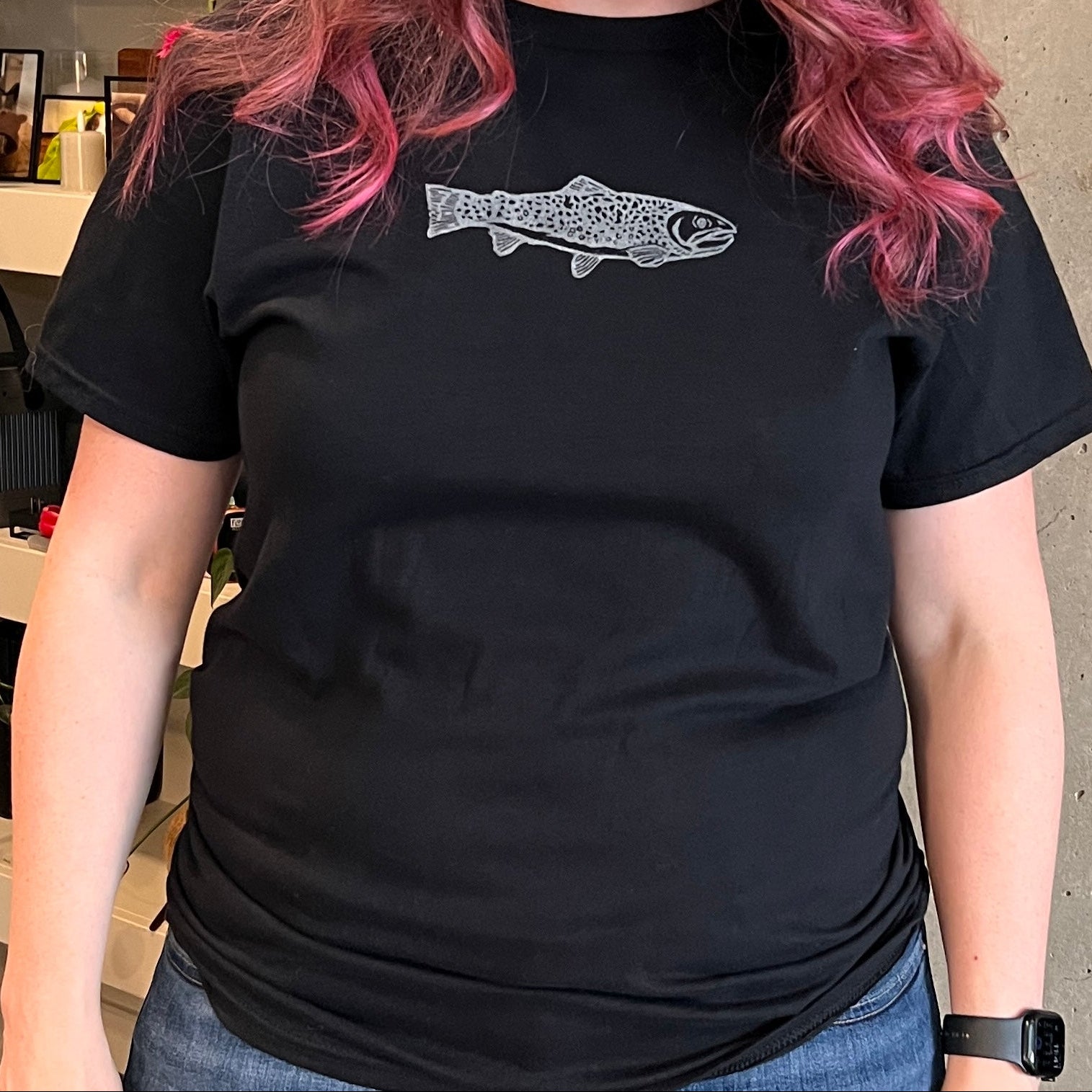 Person wearing a black t-shirt with a graphic design, standing indoors.