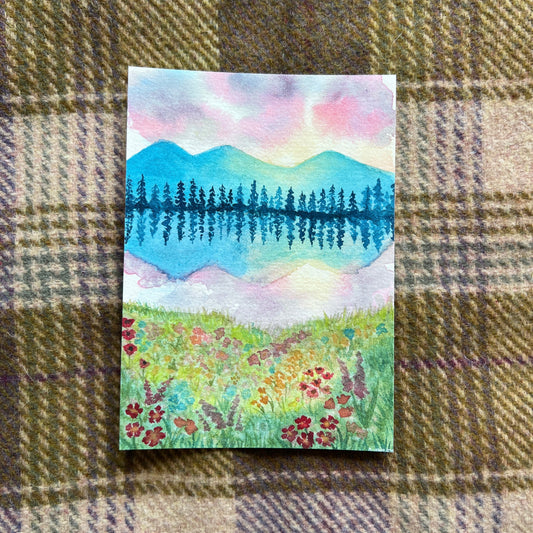 Watercolor illustration of a meadow looking over a lake with mountains and pine trees
